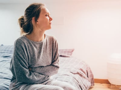 Eine Frau sitzt auf dem Bett und hält sich vor Schmerzen den Bauch.