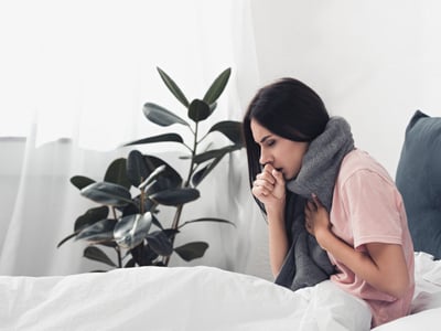 Kranke Frau sitzt im Bett und hustet.