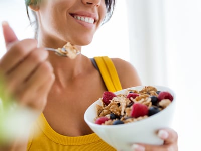 Eine junge Frau im gelben Top ist Müsli mit Beeren.