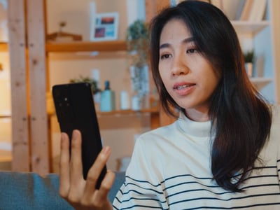Junge Frau hält Smartphone in der Hand und führt ein Videotelefonat.