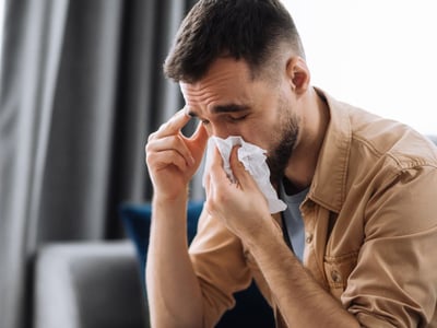 Mann mit Nasennebenhöhlenentzündung (Sinusitis) und Schnupfen schnäuzt sich in ein Taschentuch.
