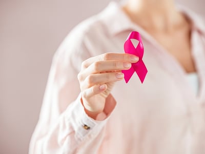 Frau hält rosa Schleife als Zeichen gegen Brustkrebs in der Hand.