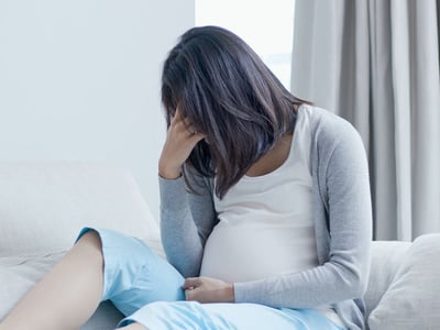 Eine schwangere Frau sitzt mit gesenktem Kopf auf dem Sofa.