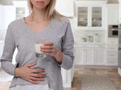 Laktoseintoleranz: Frau hält Glas mit Milch in der einen Hand, mit der anderen Hand hält sie ihren schmerzenden Bauch.