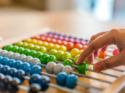 Eine Hand schiebt bunte Perlen zur Berechnung mithilfe eines Abakus hin und her.