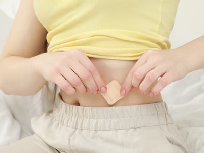 Eine Frau klebt sich ein Pflaster zur Empfängnisverhütung auf den Bauch.