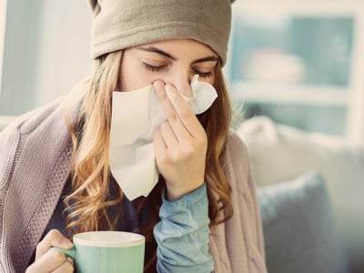 Eine Frau schnäuzt sich während sie eine Teetasse in der Hand hält.