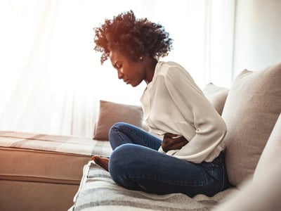 Frau mit Unterleibsschmerzen auf Sofa.