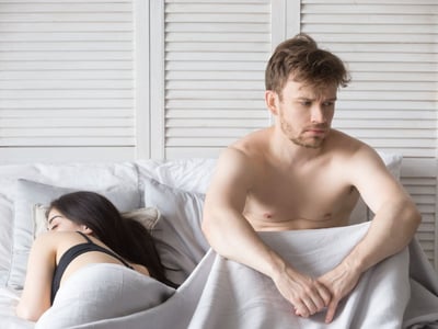 Mann und Frau im Bett. Die Frau schläft, der Mann ist wach und frustriert.