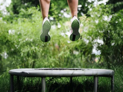 Beine beim Hochspringen auf einem Trampolin im Grünen.