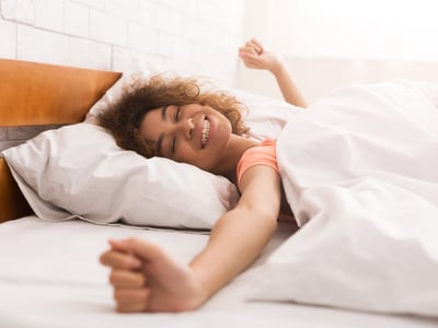 Eine junge Frau ist gerade aufgewacht ist und streckt sich im Bett.