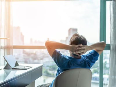 Mann im Büro lehnt sich im Stuhl zurück und blickt in die Skyline.