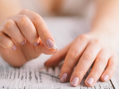 Weibliche Hand hält eine kleine runde Pille.