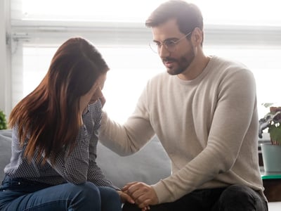 Mann sitzt mit besorgter Frau auf dem Sofa und Mann beruhigt sie