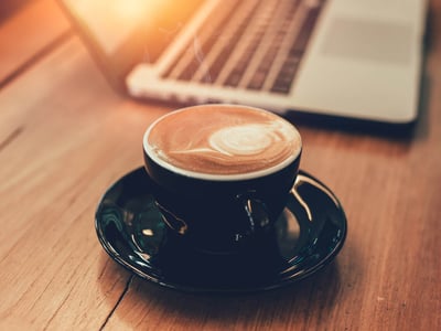 Tasse mit Kaffee neben einem Laptop auf einem Holztisch.