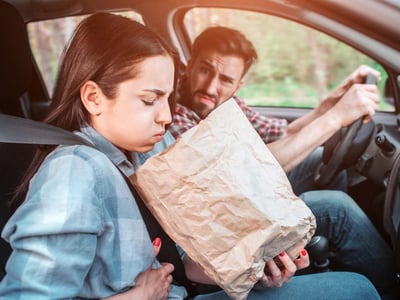 Frau leidet unter Reiseübelkeit und übergibt sich im Auto in eine Tüte.