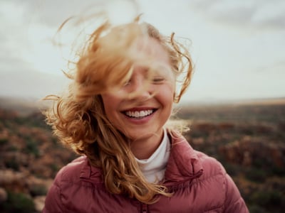 Eine lachende Frau mit rotblonden, wehenden Haaren und geschlossenen Augen.