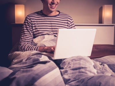 Glücklicher Mann mit Laptop im Bett.