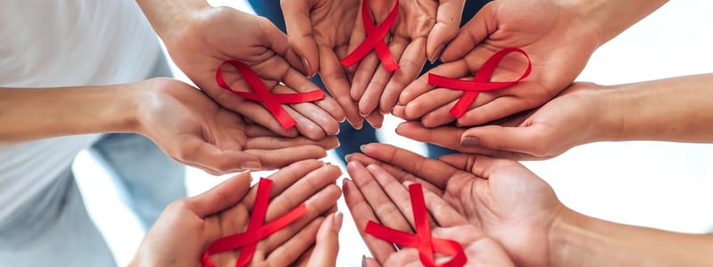 Zum Welt AIDS Tag: Solidarität mit den Betroffenen. Viele Hände halten rote Schleifen.