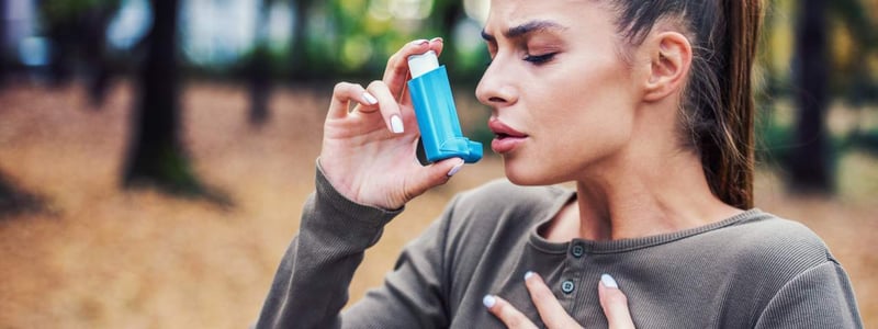 Eine junge Frau steht im Wald und benutzt Asthmaspray.