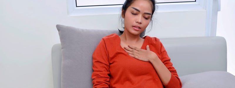 Junge Frau sitzt mit Brustschmerzen und Atemnot auf dem Sofa.