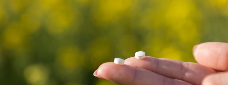 Zwei kleine weiße Tabletten werden auf den Fingerspitzen gehalten.