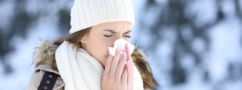 Eine Frau mit winterlicher Kleidung und Schnee im Hintergrund putzt sich die Nase.
