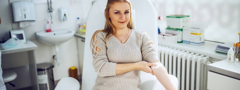 Eine junge Frau hat soeben Blut gespendet. Sie hat ein Pflaster auf dem Arm und übt mit einer Hand Druck auf die Einstichstelle aus.