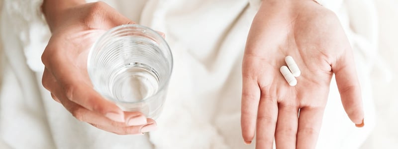 Antibiotika Tabletten in Hand und ein Glas Wasser dazu.