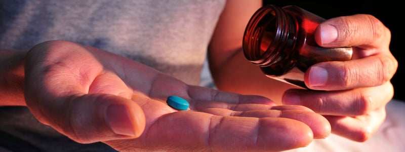Aus einer Glasflasche schüttet ein Mann sich eine blaue Tablette auf die Handfläche.