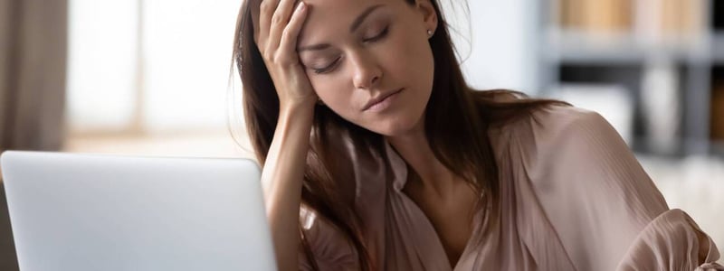 Müde Frau mit aufgestütztem Kopf vor dem Laptop.