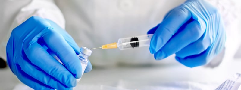 Hände mit blauen Handschuhen bereiten eine Spritze mit Impfstoff vor.