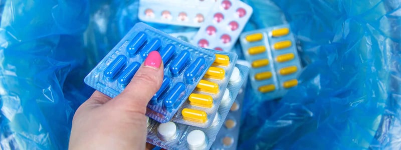 Eine Frauenhand wirft mehrere Tabletten in einen Mülleimer.