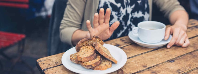 Eine Frau trinkt Kaffee und lehnt das angebotene Brot ab.