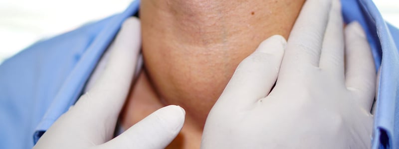 Hände mit Latexhandschuhen tasten eine vergrößerte Schilddrüse ab.