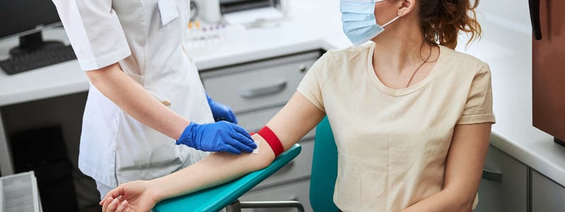 EIne Arzthelferin nimmt bei einer Frau Blut ab.