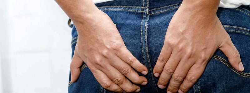 Person in Jeans hält sich den Po mit beiden Händen.