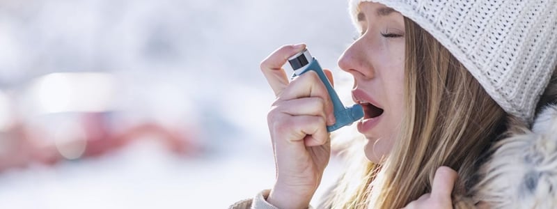 Junge Frau benutzt im Winter einen Asthma-Inhalator.