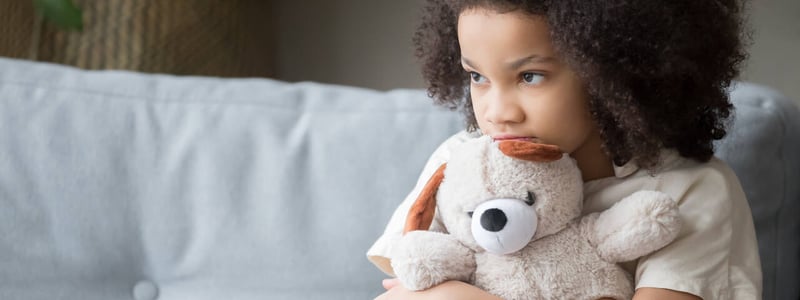 Trauriges Mädchen mit Teddybär auf Sofa.