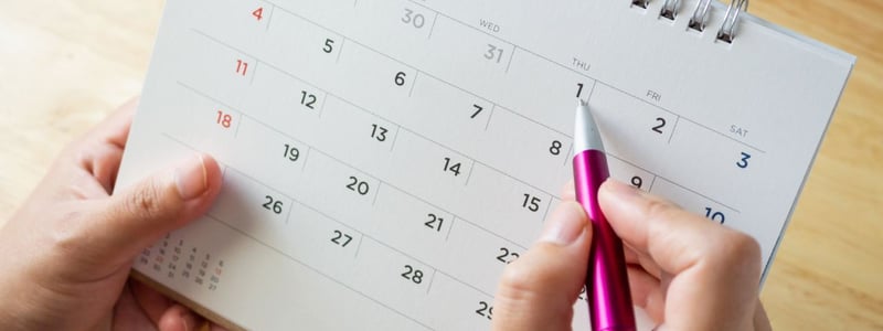 Auf einem Kalender werden mit einem Stift Daten eingetragen.