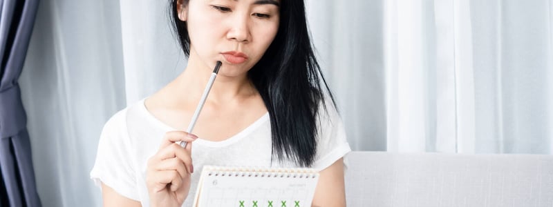 Frau betrachtet mit Stift am Mund ihren Kalender.