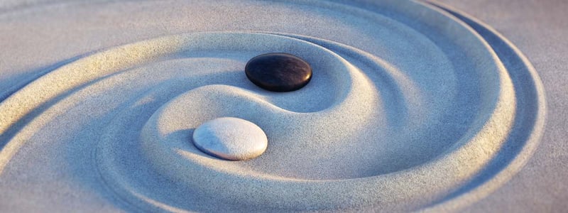 Ying und Yang wurde in den Sand gezeichnet. Die Symbolik wird durch einen schwarzen und einen weißen Stein verdeutlicht.