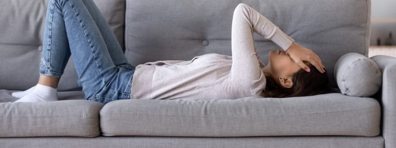 Eine Frau hat vestibuläre Migräne und liegt mit Kopfschmerzen und Schwindel auf dem Sofa.