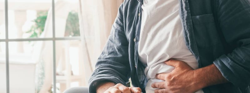 Ein Mann hält sich im Sitzen vor Schmerzen den Bauch.