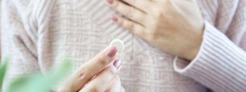 Frau hält mit der einen Hand die schmerzende Brust und in der anderen Hand eine Tablette.