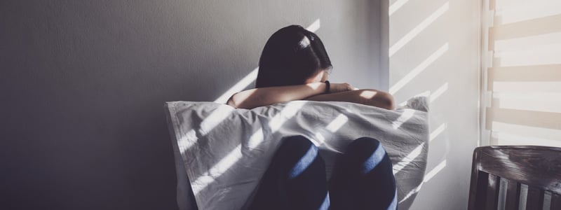 Junge Frau mit Migräne sitzt mit Kopfschmerzen und Übelkeit in einem abgedunkelten Raum.