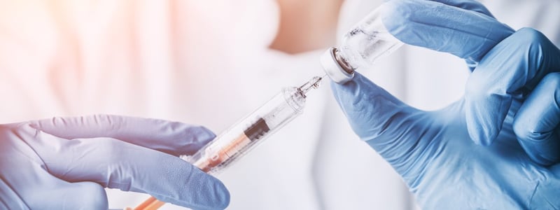 Eine Ärztin mit Handschuhen entnimmt Impfstoff aus einem Fläschchen mit einer Spritze.