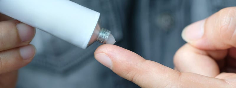Ein Mann drückt Salbe aus einer Tube auf seine Fingerspitze.