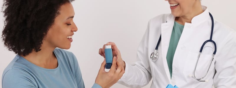 Eine Ärztin reicht einer Patientin mit Asthma einen Inhalator.