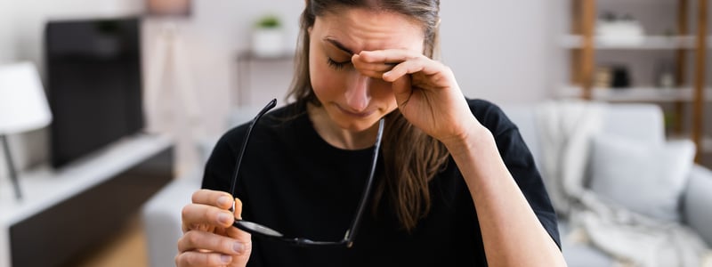 Frau am Schreibtisch hält eine Brille in der Hand und reibt sich die Augen.